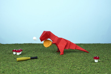 Tiranosaurio rex rojo de origami jugando al béisbol como lanzador. ¡Diversión al aire libre!
