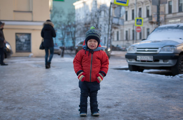 Little boy in a red jacket crying in the street.