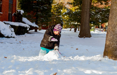 Fototapeta na wymiar Funny little girl in a warm winter outfit, building snow man. Kid playing outdoors in .