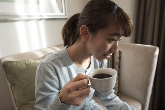A young woman is sitting on a sofa and drinking coffee