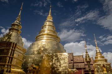 Fototapeta premium Low angle view of gold pagoda with golden chedi at Wat Phra Singh temple in Chiang Mai, Thailand, with amazing cloudy sky background