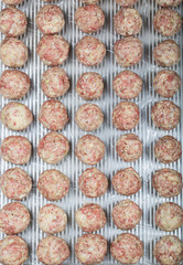 Rows of raw meatballs on a sheet. Overhead shot