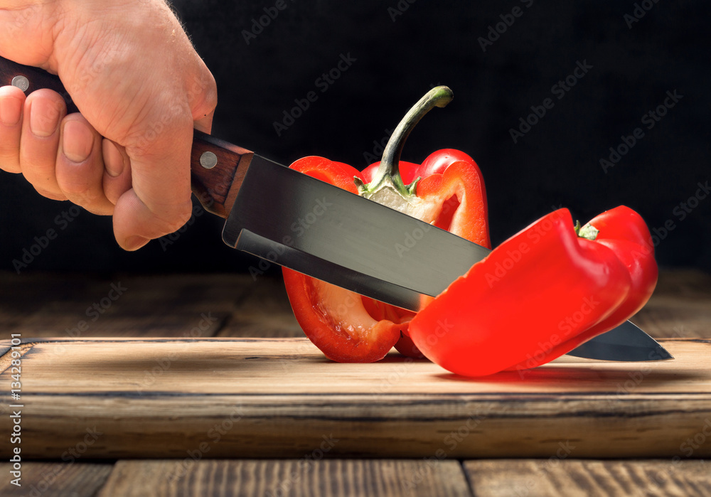 Wall mural man's hand with a kitchen knife cuts red pepper