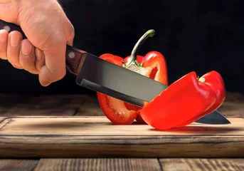 Poster Man's hand with a kitchen knife cuts red pepper © kucherav