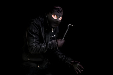 Masked thief in balaclava with crowbar isolated on black