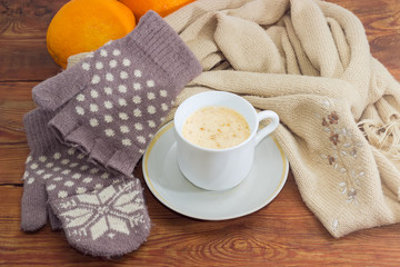 Coffee with cream on background of woolen mittens and scarf