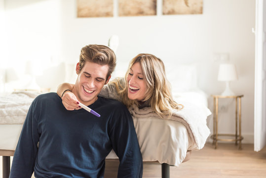 Happy couple looking at pregnancy test on bed
