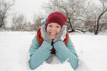 Portrait of a cute young woman having fun in snow in winter park. young woman lying on the snow
