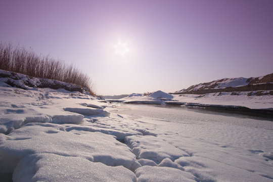 Snowy frozen river with cracked ice on a sunset background