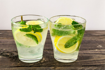 Two glasses of Fresh sweet cold carbonated homemade lemonade with lemon slices and mint leaves on old dark grey rustic wooden table.
