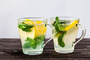 Two glasses of Fresh sweet cold carbonated homemade lemonade with lemon slices and mint leaves on old dark grey rustic wooden table.
