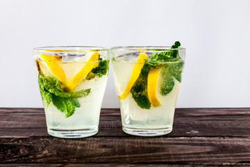 Two glasses of Fresh sweet cold carbonated homemade lemonade with lemon slices and mint leaves on old dark grey rustic wooden table.
