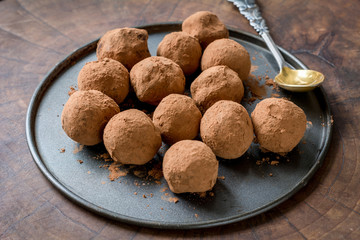 Chocolate truffles rolled with cocoa powder on a plate over wooden background.