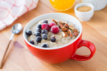 Oatmeal porridge with cranberries, black currant and almonds in red bowl on wooden table. Healthy breakfast food. Concept of clean eating, vegan, vegetarian and diet meal. Morning shot