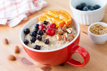 Oatmeal porridge with cranberries, black currant, orange and almonds in red bowl on wooden table. Healthy breakfast food. Concept of clean eating, vegan, vegetarian and diet meal. Morning shot