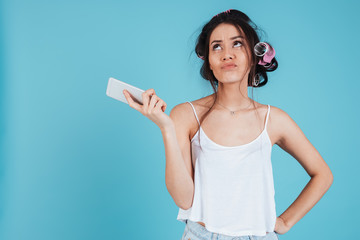 Confused young woman with hair curlers using phone