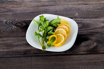 Slices of fresh juicy lemon with mint leaves on small plate on old dark grey rustic wooden table. Top view. Ingredients for homemade lemonade cocktails, mojito.
