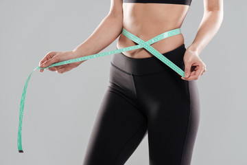 Closeup of fitness woman standing measuring her waist with tape