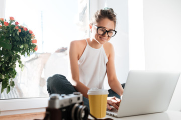 Cheerful woman photographer in glasses working with laptop at home
