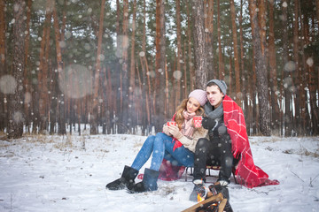 Fototapeta na wymiar Loving couple in the winter under a blanket with a cup of hot coffee or tea, it's snowing
