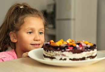 Cute little girl going to taste sweet cake left on kitchen table