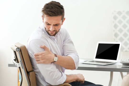 Handsome young man suffering from shoulder pain in office