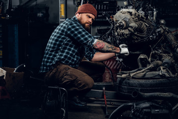 Bearded male repairing car's engine in a garage.