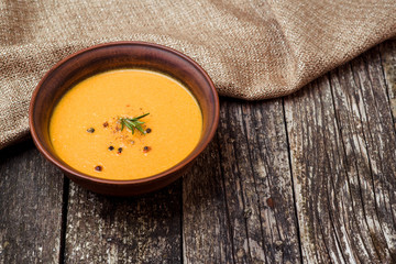 Bowl of pumpkin soup with bread crouton on dark wooden table.
