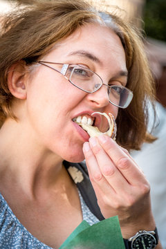 Portrait of woman in glasses  taking a bite and eating pastry outdoors.