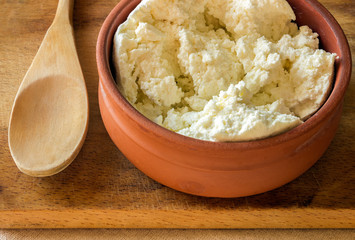 Fresh cottage cheese in a ceramic bowl. Wooden spoon .