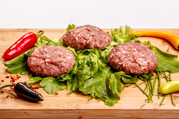 Raw beef burgers with peppers and greens are on the Board.