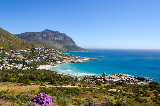Coastline of Camps Bay near Cape Town in South Africa on a beautiful summer day with quite ocean and blue sky extending to the horizon. Beautiful vegetation beach and homes right of the coast