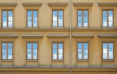 old yellow building with windows reflection of clouds in them