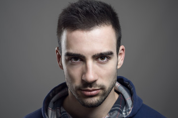Close up portrait of angry young bearded male wearing hoodie staring at camera