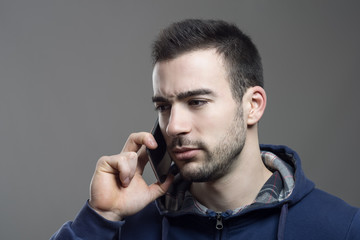 Serious upset young stubble man listening on the cellphone 