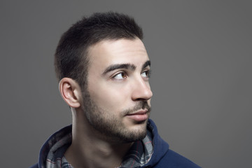 Handsome young stubble man looking up. Close up portrait over gray studio background. 