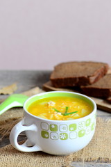 Chicken rice soup with potatoes, green onions and carrots in a bowl. Bread slices, burlap textile, spoon on wooden table. Homemade soup recipe. Vertical photo. Closeup