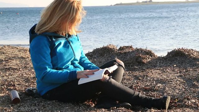 Middle aged woman warmly clothed on the beach in autumn, relax and reading book