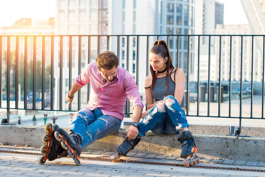 Young couple on rollerblades sitting. Two people on urban background. First date in the city.