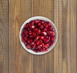 Pomegranate seeds on a wooden background. Red grains of a pomegranate in ceramic bowl. Top view.