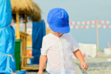 Baby boy in blue cap with sad expression. Frown baby boy on the stone beach in summer vacation