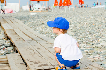 Boy in blue cap with sad expression. Resent and crouch. Frown baby boy on the stone beach in summer vacation