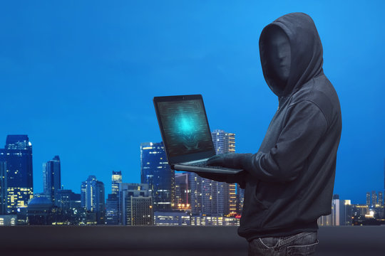 Hooded hacker with anonymous mask typing on laptop