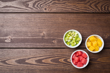 Cut fruits in white bowls on wooden table