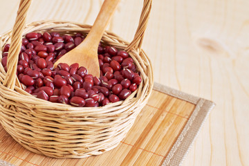 Raw adzuki red beans in woven basket on wooden background. Copy space