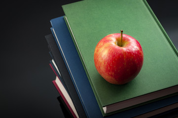 Back to school concept with an apple on top of a stack of books arranged in a tower and copy space