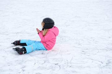 Fototapeta na wymiar Child girl sitting on ice after falling in snowy park during winter holidays 
