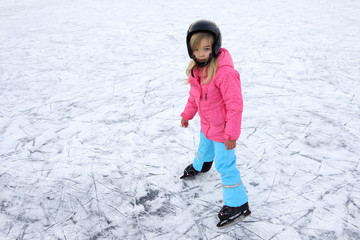 Fototapeta na wymiar Happy little girl skating in winter outdoors, wearing safety helmet 