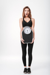 Shocked young fitness lady holding scales