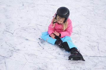 Child girl sitting on ice after falling in snowy park during winter holidays 